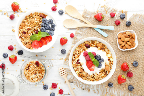 Tasty granola with fresh berries and spoons on white wooden background