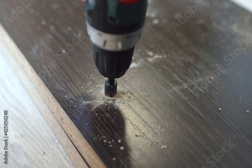 In purple, a man drills a hole in a blank for laminating MDF furniture. MDF furniture assembly concept