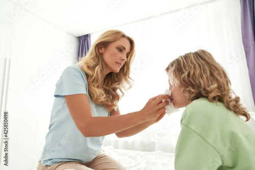 A picture of a mother blowing her son's nose in bedroom