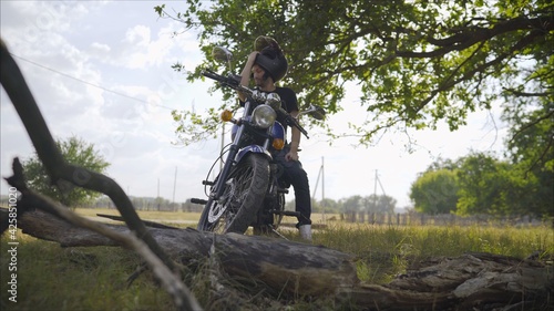 A man on a motorbike against the sea. Motorcyclist stands under a tree. Motorcyclist with a motorcycle in the summer in a clearing.