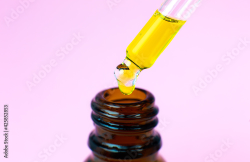 Bottle of cosmetic oil with a pipette on a pink background. Close up liquid drop dripping. Beauty, medicine and  health care concept. Macro photo. Natural, eco cosmetics.