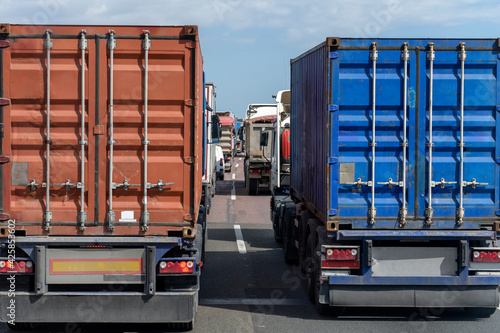 Dos contenedores azul y rojo en un atasco en la autopista de la carretera tras una fila de varios camiones y otros vehículos.