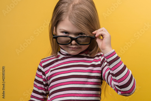 Fototapeta Naklejka Na Ścianę i Meble -  Children's cinema concept. White girl in 3D glasses with different emotions on a yellow background.