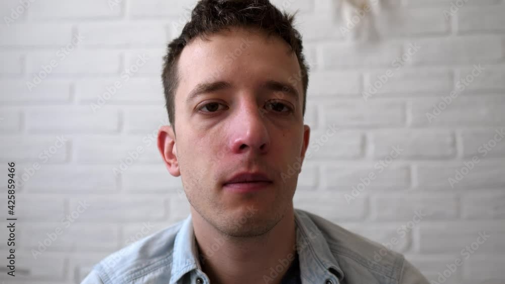 Sick guy is sitting on the bed and he has a runny nose. A man has the flu, a virus, or an allergy. Healthy medicine and people concept. Allergies, runny nose and sneezing. Blowing nose. Sick guy is sitting on the bed and he has a runny nose. A man has the flu, a virus, or an allergy. Healthy medicine and people concept. Allergies, runny nose and sneezing. Blowing nose.