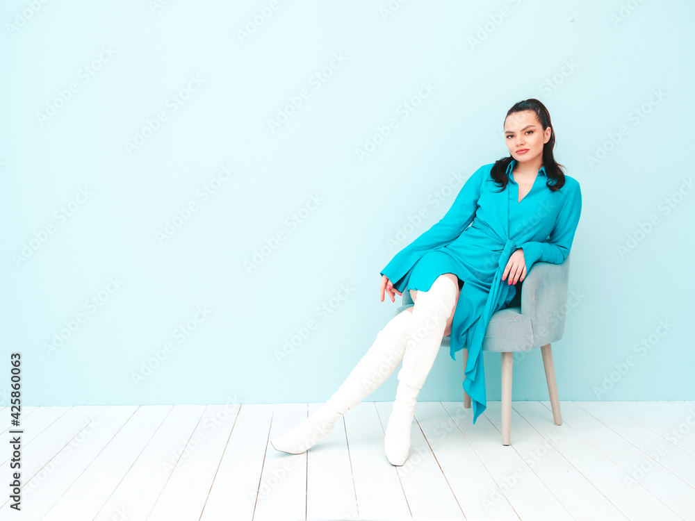 High fashion portrait of young beautiful brunette woman wearing nice trendy summer dress.Sexy fashion model posing near light blue wall in studio.Fashionable female sitting in chair High fashion portrait of young beautiful brunette woman wearing nice trendy summer dress.Sexy fashion model posing near light blue wall in studio.Fashionable female sitting in chair
