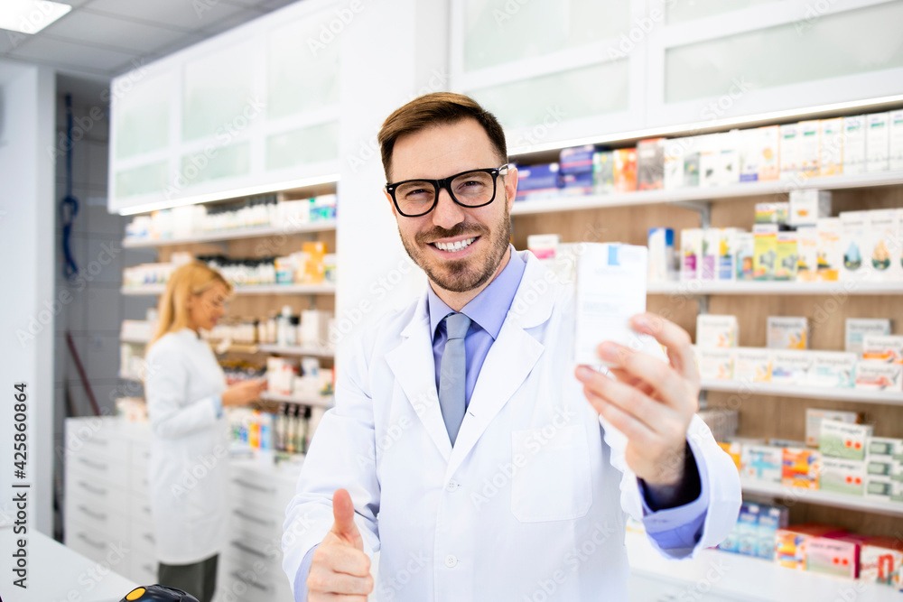 Portrait of smiling caucasian pharmacist holding vitamins in drug store.