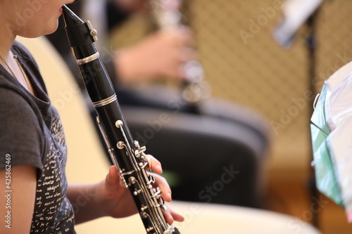 Fototapet Close-up of a baby girl playing a black clarinet mouthpiece in her mouth fingers on silver flaps in a music lesson at school