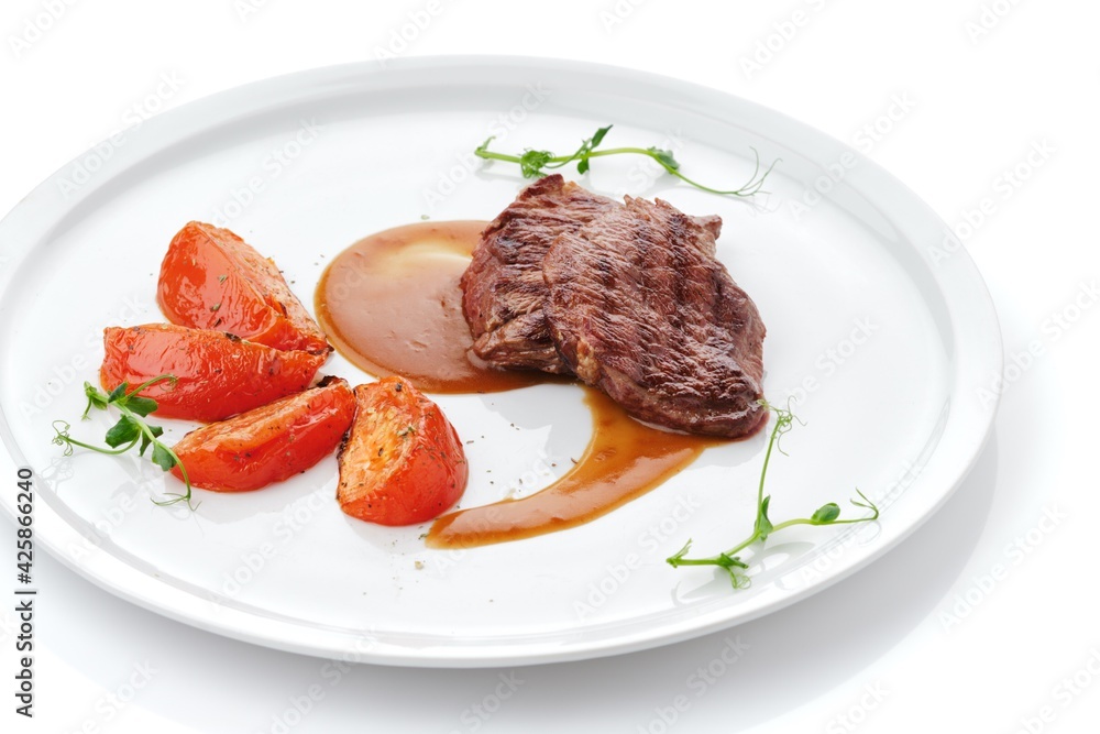 Grilled sliced Beef Steak with sauce, tomatoes and green on a white plate. Top view.