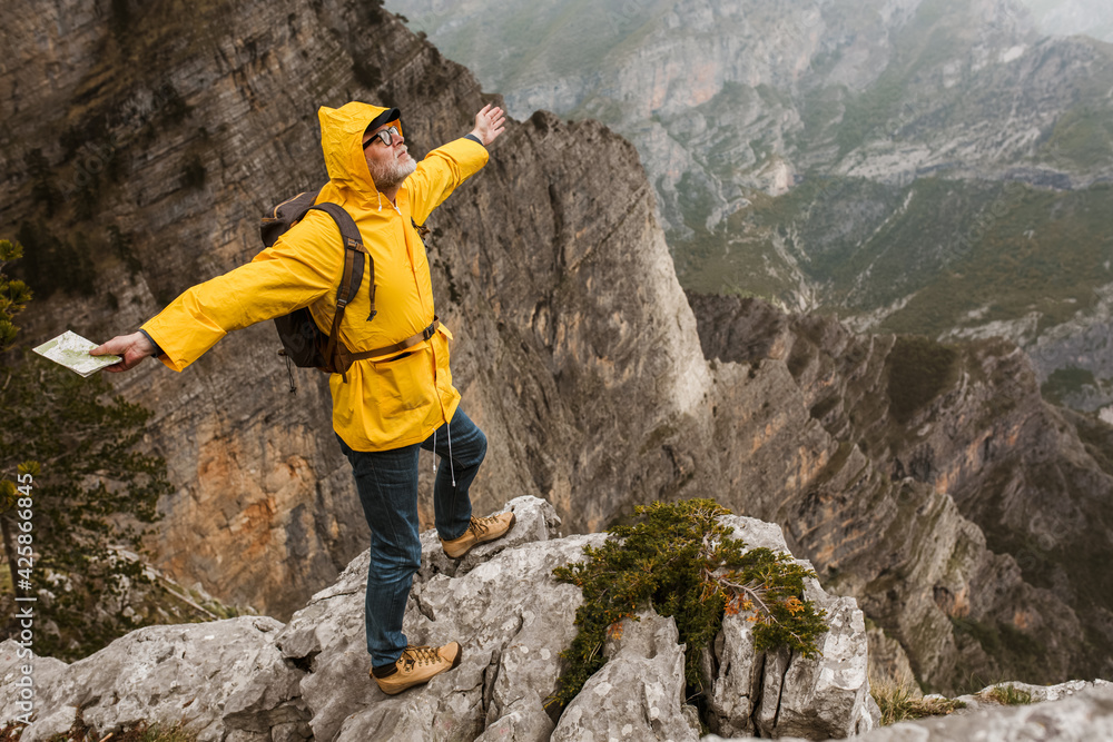 Middle age man traveler in raincoat and backpack enjoying view of mountains.
