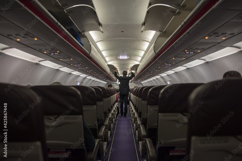 A steward closing compartments in a cabin; View from the back of an almost empty airplane during corona crisis with only a few passengers on board before departure A steward closing compartments in a cabin; View from the back of an almost empty airplane during corona crisis with only a few passengers on board before departure