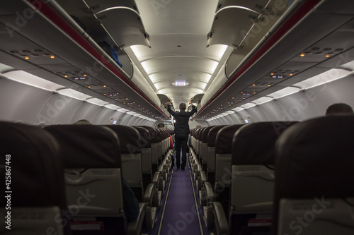 A steward closing compartments in a cabin; View from the back of an almost empty airplane during corona crisis with only a few passengers on board before departure