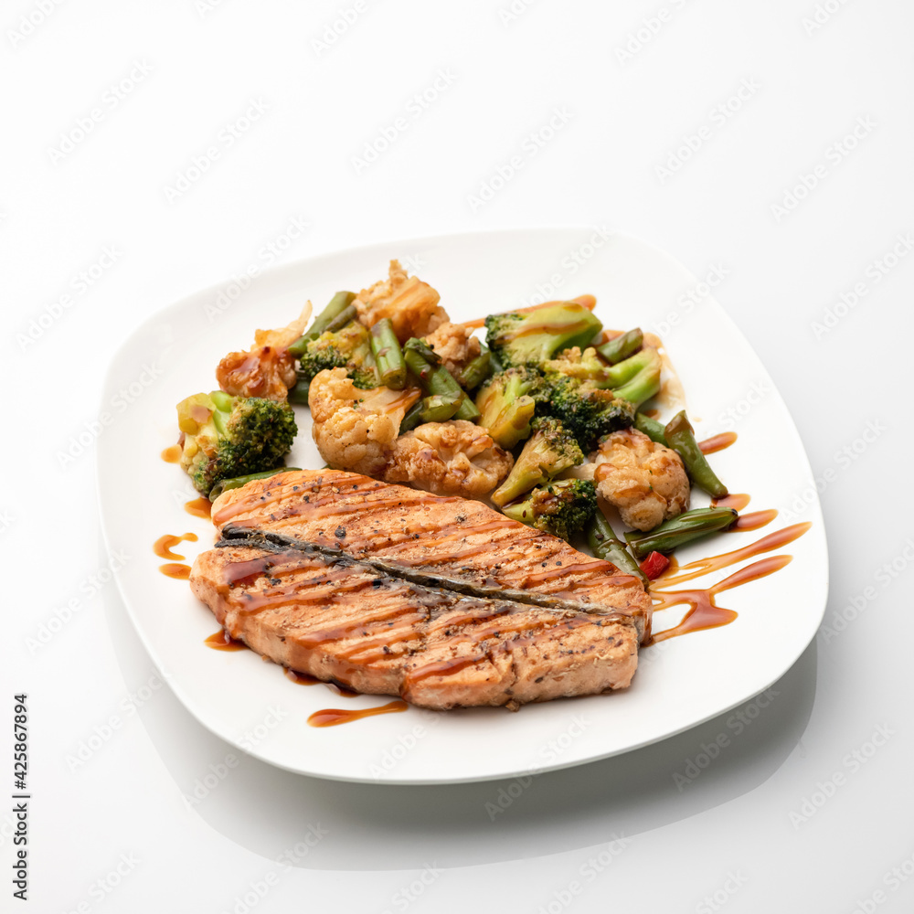 Red fish cooked with vegetables. Seafood plate isolated on white background. Sea or river salmon or trout baked or fried with broccoli and cauliflower.