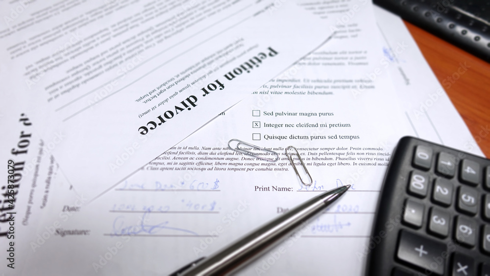 Blurred divorce contract papers with the husband signing it. Conceptual image for divorce with calculator and a hand signing the contract. Shallow depth of field with selective soft focus on the pen. Blurred divorce contract papers with the husband signing it. Conceptual image for divorce with calculator and a hand signing the contract. Shallow depth of field with selective soft focus on the pen.