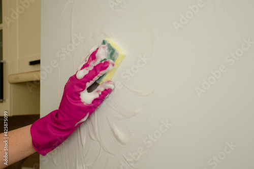 Womens hands in rubber gloves wash white refrigerator with a sponge and foam. Housework and cleaning concept