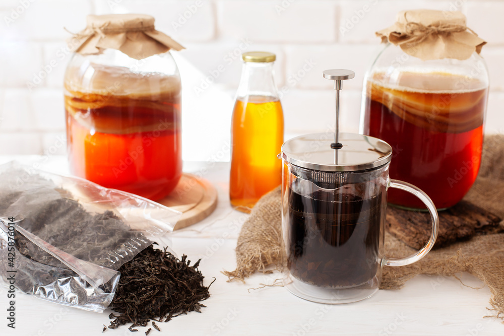 Fototapeta premium Set for preparing homemade fermeted drink. Glass jar with scoby, bottle with ready komucha and black tea brew. Light bricked background.