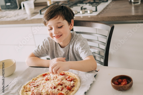 Little kid boy making pizza sitting at the table on the kitchen. Children helping in cooking lifestyle image