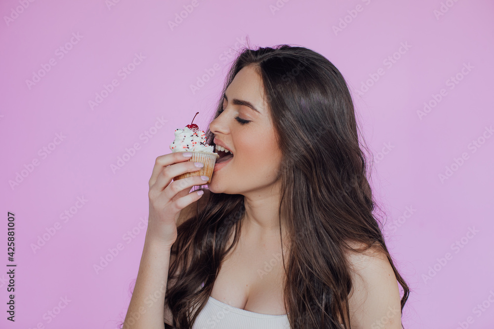 Portrait of a seductive young girl with bright makeup over violet background, eating cupcake
