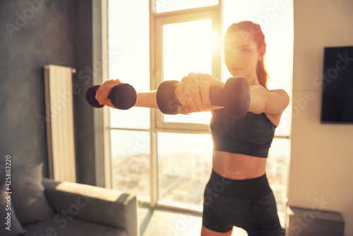 Young gym woman training exercises at home with dumbbells