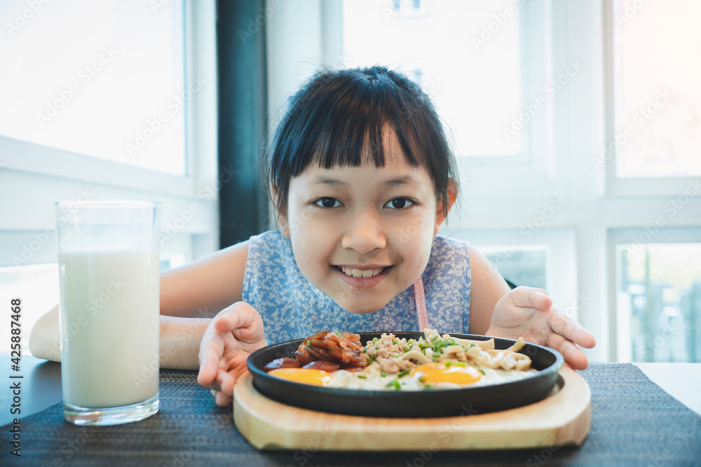 Asian little girl smiling with fried egg and fresh milk in breakfast Asian little girl smiling with fried egg and fresh milk in breakfast
