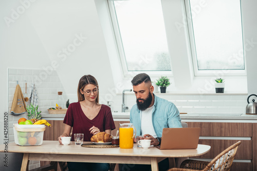 Couple having breakfast while using a laptop at home