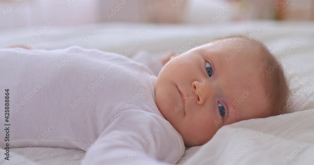 Portrait, a newborn baby lies on a white bed, big blue eyes. Little ones move their arms and look around carefully. 4k, ProRes Portrait, a newborn baby lies on a white bed, big blue eyes. Little ones move their arms and look around carefully. 4k, ProRes