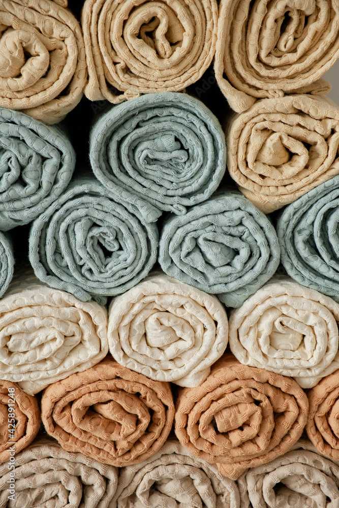 Home towels made of natural muslin in pastel shades are folded neatly in a row and decorated with a rope with a bead. Natural, soft and stylish home textiles. Grey background. View from above. Home towels made of natural muslin in pastel shades are folded neatly in a row and decorated with a rope with a bead. Natural, soft and stylish home textiles. Grey background. View from above.