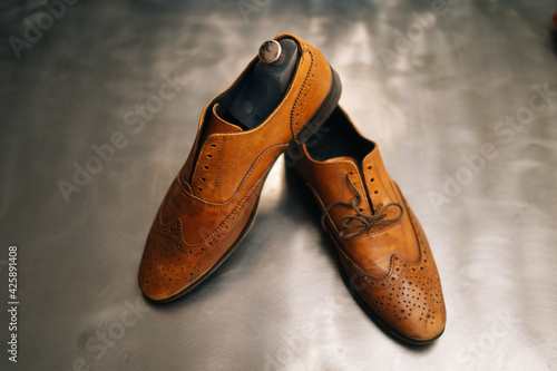 Quadro em tela Close-up top view of old light brown leather shoes with wooden shoe pad to be repaired in dark craft shoe shop