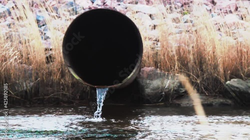 Runoff of excess water through large-diameter pipe from water reservoir. In background is dam of granite blocks photo
