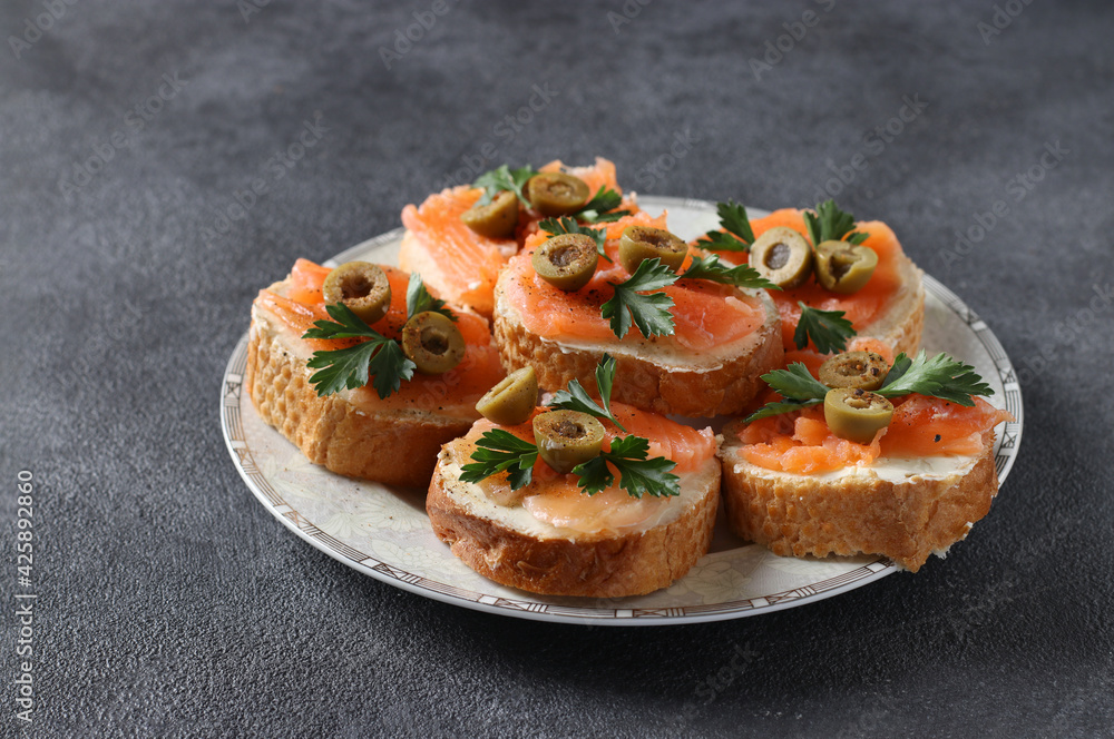 Canapes of salted salmon, green olives and parsley on croutons of white bread on dark gray background. Festive snack. Canapes of salted salmon, green olives and parsley on croutons of white bread on dark gray background. Festive snack.