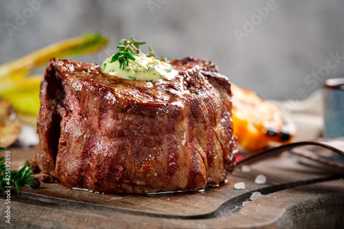 Large grilled Filet Mignon steak with butter and thyme served on a wooden board. Roast tenderloin dish, close up photo