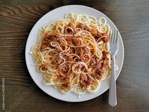 Spaghetti Bolognese with minced beef, onion, chopped tomato, garlic, olive oil, stock cube, tomato puree and Italian herb. Traditional Italian food on a white plate with a fork on the right. 