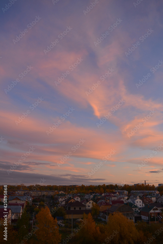 Beautiful landscape with town in autumn evening. Pink clouds in blue sky, houses and trees with golden foliage Beautiful landscape with town in autumn evening. Pink clouds in blue sky, houses and trees with golden foliage