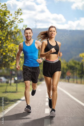 Young man and woman jogging on a running asphalt lane in the city