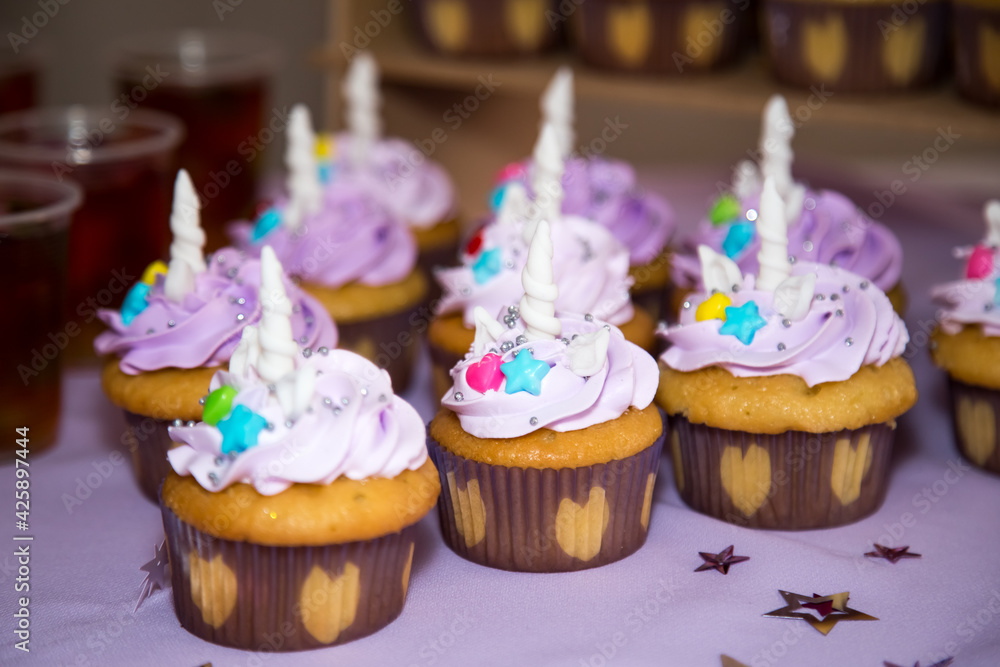 Tasty Vanilla Buttercreme Iced Cupcakes with unicorn horns ears and colored candy toppers in hearted design paper wrap for party dessert. Perfect for Holydays and especial occasions