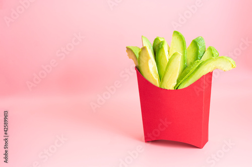 Fresh avocado slices snack, abstract concept of healthy fries in green papper box on pink background photo
