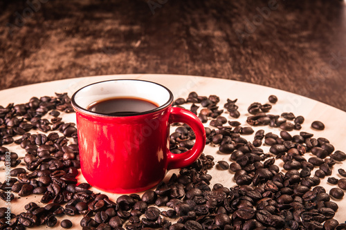 Red cup of coffee with coffee beans around on a wooden board on a wooden table.