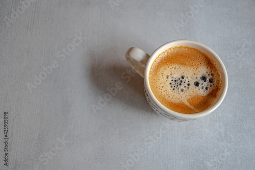 A cup of coffee in the morning light with an appetizing froth on a ceramic gray surface.