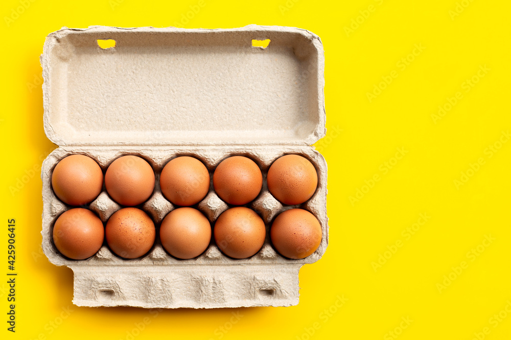 Chicken eggs in egg box on yellow background.