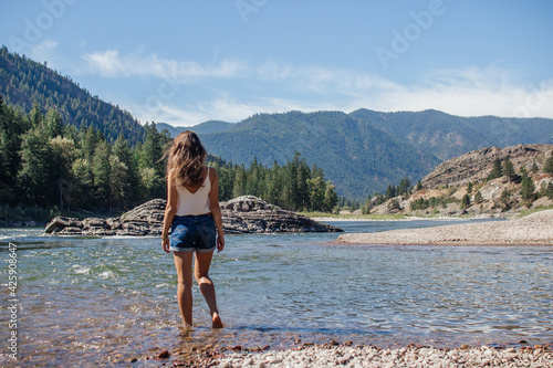 A young woman walks along a mountain river in the forest.Beautiful landscape with mountains,forest,and river with large rocks on a sunny summer day.Rest Area, I-90, Alberton, Montana, USA