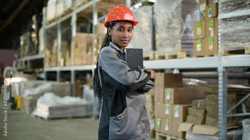 Portrait of a young black woman at work. Worker of production and warehouse in overalls and orange helmet Portrait of a young black woman at work. Worker of production and warehouse in overalls and orange helmet