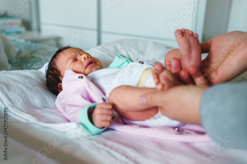 Mother taking care of her baby infant boy or girl while lying on bed at home in day - motherhood concept real people caucasian woman with her small son or daughter changing clothes