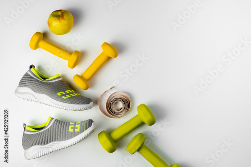 Gym and workout   sports shoes  sneakers  Healthy lifestyle concept foto. Flat lay of sport. Athlete s set with centimeter tape  green apple and dumbbells on a grey background