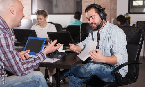 Young bearded man sharing business ideas with his senior colleague in open plan office. Concept of teamwork