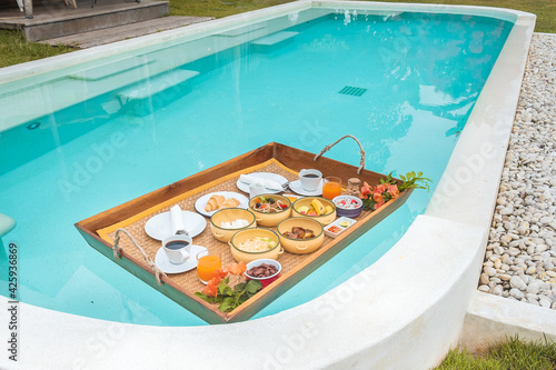 Floating Breakfast tray in swimming pool at luxury hotel or tropical resort villa, fruits, croissant, coffee, and orange juice. Exotic summer, relaxation, tropical travel and vacation concept © Jo Panuwat D