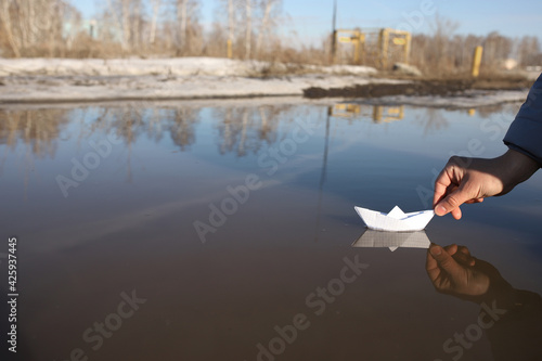 A man launches a boat out of paper in a puddle in the spring. A boat floats from a notebook sheet in a puddle.