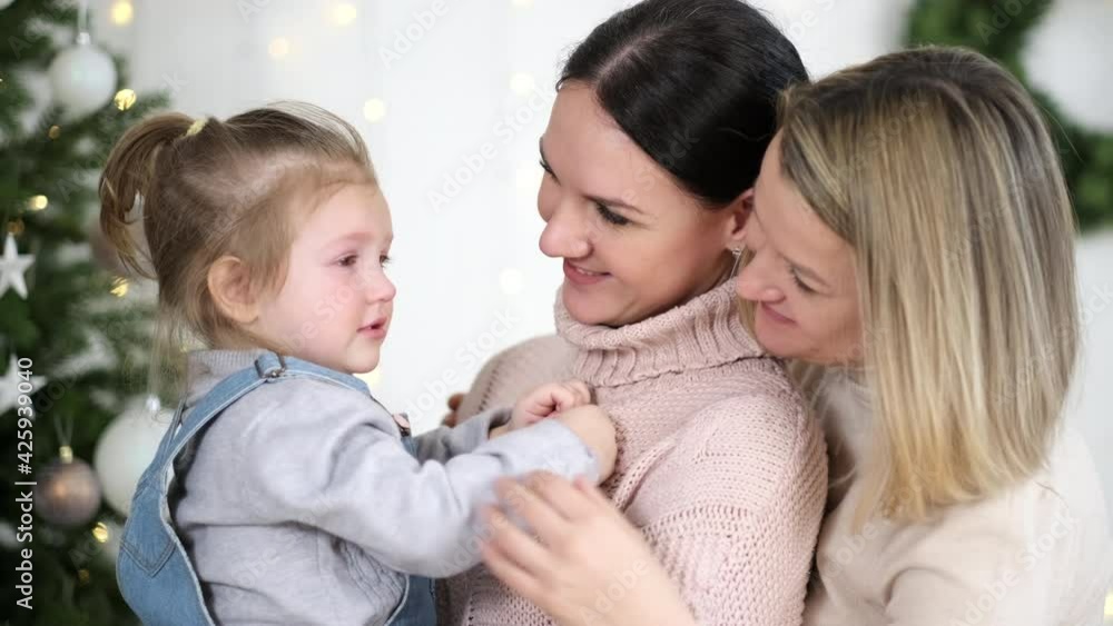 Two mothers and a young daughter spend time at home. They're playing on the window sill. Warm home clothes. Lgbt family, lesbians with a child. Two mothers and a young daughter spend time at home. They're playing on the window sill. Warm home clothes. Lgbt family, lesbians with a child.