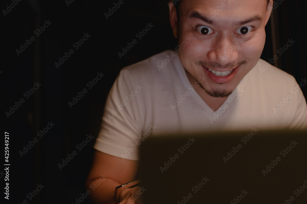 Shocked and surprised funny face of Asian man watch the laptop alone at night. Shocked and surprised funny face of Asian man watch the laptop alone at night.