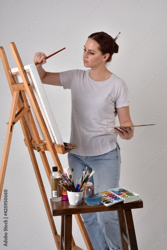 Close up portrait of a red haired artist girl wearing casual clothes. standing pose
painting a canvas on an easel, against a studio background. Close up portrait of a red haired artist girl wearing casual clothes. standing pose
painting a canvas on an easel, against a studio background.