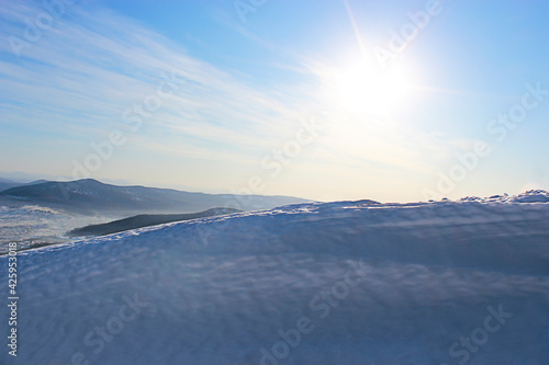 Winter landscape. Snowdrift against the background of mountains and blue sky and shining sun © Алена Ягупа