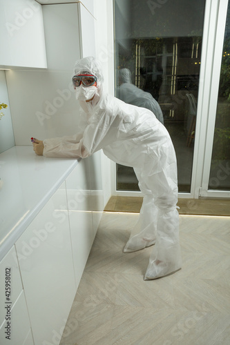 medical adviser wearing covid-19 protection suite, gloves, breather and protective glass stands near aumbry with test-glasses in her hands photo